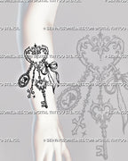 Antique key and charm tattoo shown on the forearm with a long skeleton key, ribbon bow, filigree heart ring, cameo, and dangling chains