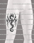 Blackwork winged dragon tattoo shown on a man’s front thigh with horned fantasy head, broad wings, fragmented tribal shapes, sharp points, and curled tail