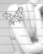 Filigree butterfly tattoo shown on a woman’s upper arm with ornate baroque wings, botanical curls, and a jewelry-inspired pendant