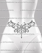 Filigree dragonfly tattoo shown across a woman’s lower back and waist with symmetrical baroque wings and a hanging ornament aligned at the center