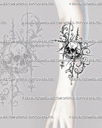 Filigree skull tattoo shown on the forearm with a detailed skull, curling baroque scrollwork, hanging ornamental accents, and elongated spear-like points