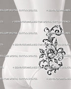 Floral filigree tattoo shown on the side of women’s lower back with a central rose, asymmetrical baroque scrollwork, botanical leaves, and flowing curls