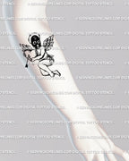 Masked cupid tattoo stencil shown on forearm placement with black mask, heart and arrow motif, and dark angelcore style