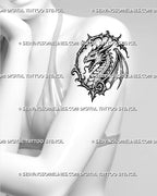 Medieval dragon head tattoo stencil shown on women’s upper arm with gothic dragon portrait, long horns, open jaw, wing detail, and pointed frame linework