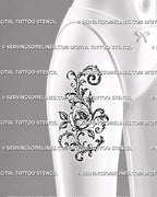 Ornamental rose filigree tattoo shown on the front of a female thigh with a large open flower, sweeping scrolls, curled leaves, and pointed decorative details
