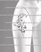 Skull lily of the valley tattoo shown on women’s front thigh with four detailed skull-shaped blooms, arching bell flowers, long leaves, and a butterfly