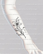 Abstract lily-inspired fluid flower tattoo stencil displayed on forearm placement, black line art flowing naturally along skin. 