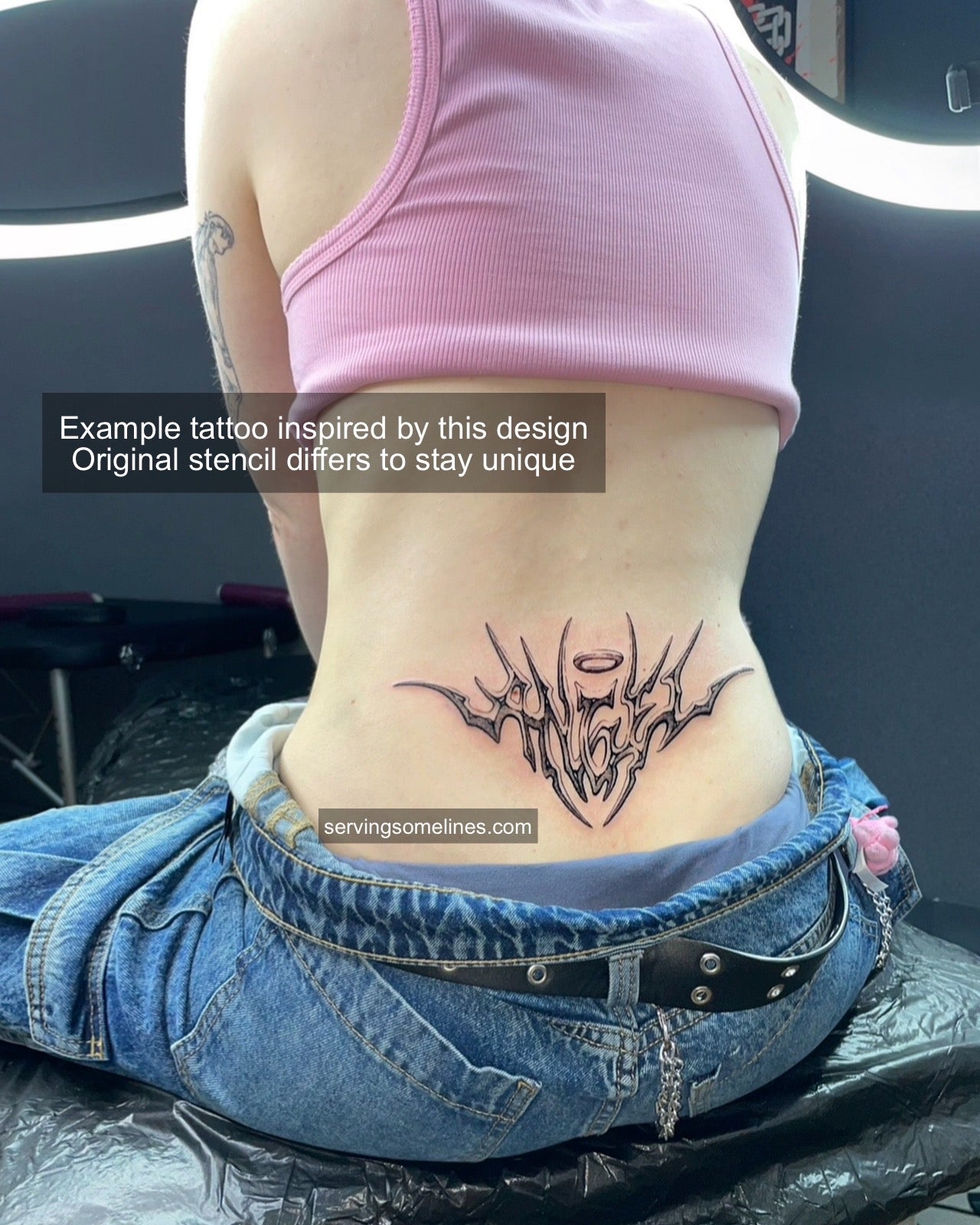 Real tattoo example of angel lettering word design on lower back, fine neotribal cyber font with halo accent and sharp symmetrical flow.